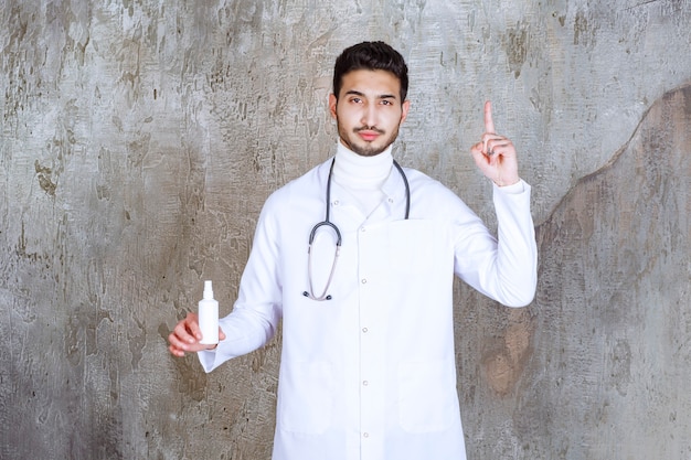 Male doctor with stethoscope holding a white hand sanitizer bottle and thinking or having a good idea