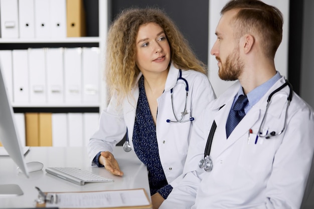 Male doctor withcolleague discussing current disease therapy while sitting at working place in clinic. Team work in medicine