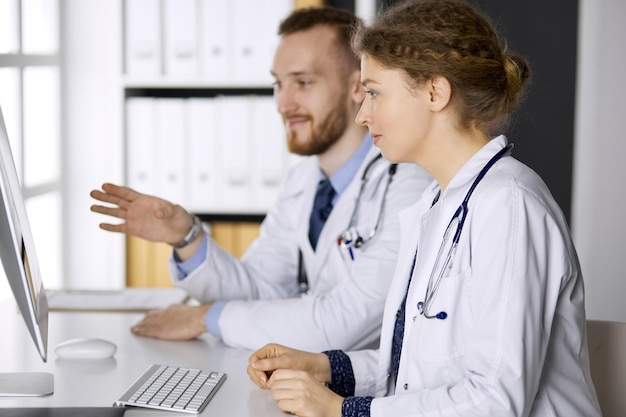 Male doctor withcolleague discussing current disease therapy while sitting at working place in clinic. Team work in medicine.