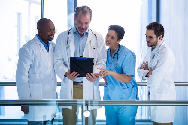 Male doctors and nurse having discussion over clipboard in corridor