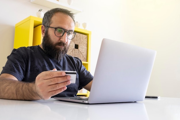 Male doing online shopping. Providing online payment at the office holding credit card.