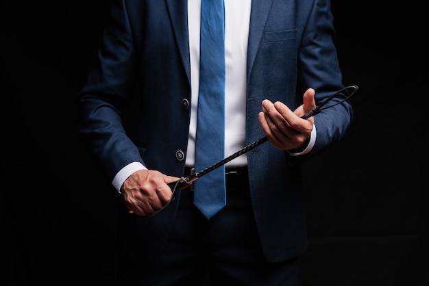 Male dominant businessman in a suit holding a leather whip Flogger for domination in BDSM sex