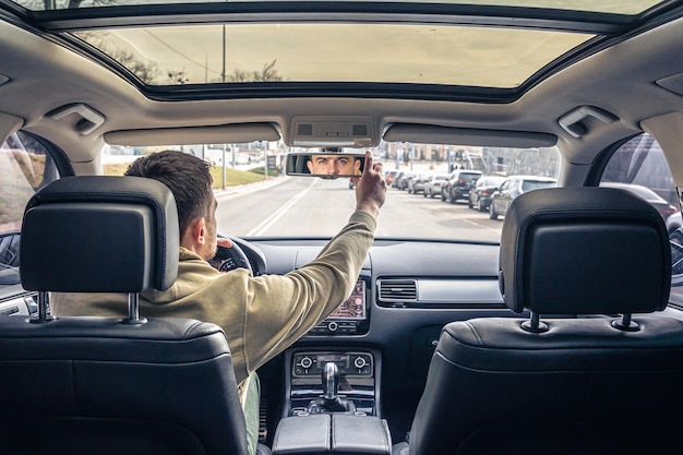 A male driver adjusts the mirror in the car