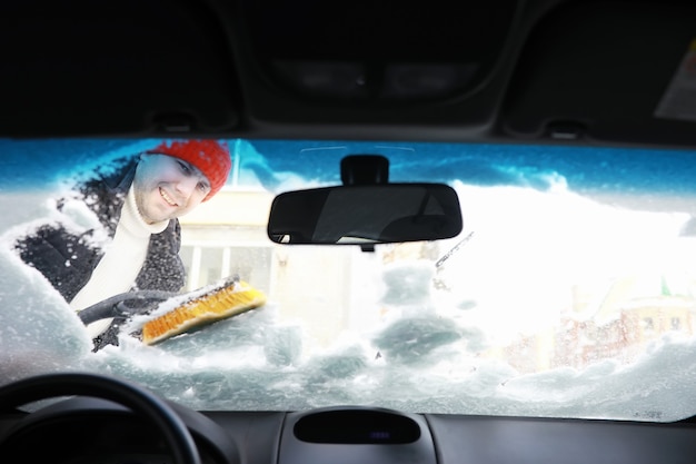 男性ドライバーが車の前に立っています。所有者は冬に雪から車を掃除します。降雪後の車。