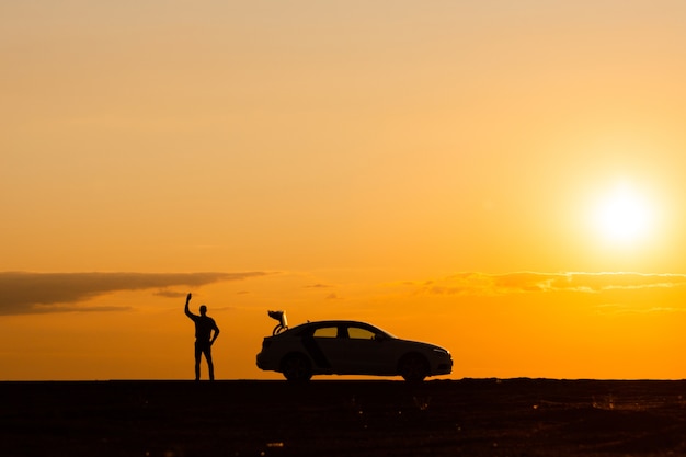 写真 男性ドライバーが手を挙げて助けを待っている、日没時に故障した後、車はそれ以上動くことができない