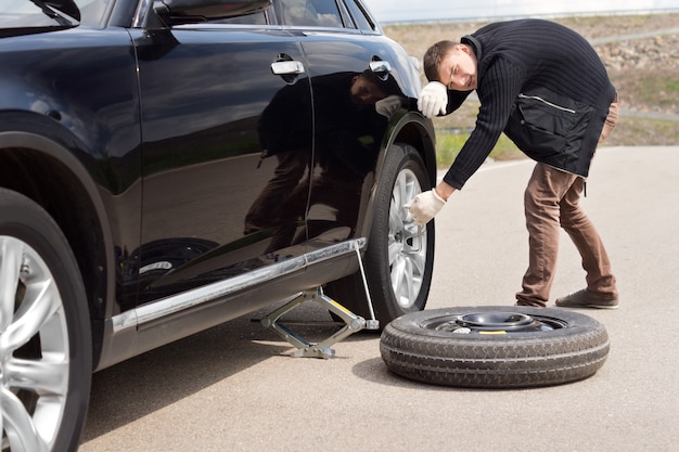 写真 車のタイヤ交換に苦労する男性ドライバー