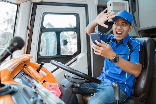 A male driver in uniform looks at his cellphone while he is carelessly driving with an expression that crashes inside the bus