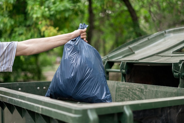 Male dumping waste package into a big trash bin containers