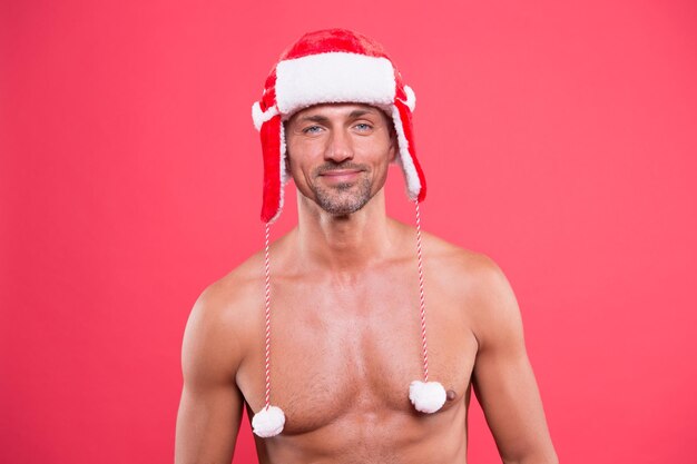 Male in earflap winter hat happy new year xmas party for adult handsome santa feel warm and hot christmas temptation best christmas present sexy santa muscular man santa hat red background