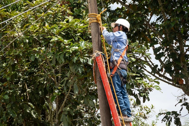 Male electrician wearing clothing helmet and safety harness\
climbing on a light pole