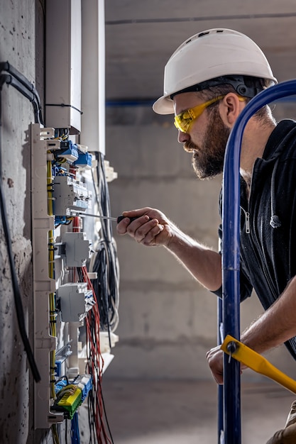 A male electrician works in a switchboard with an electrical connecting cable.