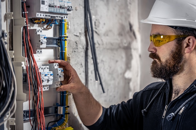 男性の電気技師は、電気接続ケーブルを使用して配電盤で作業します。