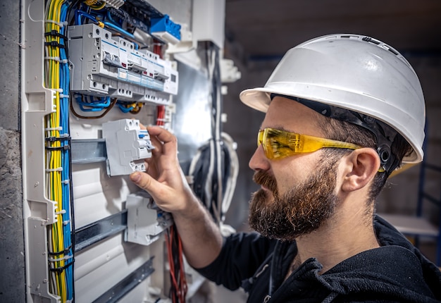 A male electrician works in a switchboard with an electrical connecting cable