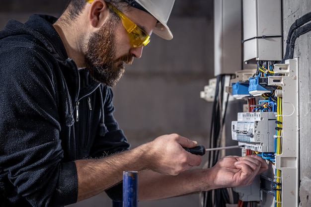 A male electrician works in a switchboard with an electrical connecting cable