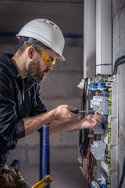 A male electrician works in a switchboard with an electrical connecting cable