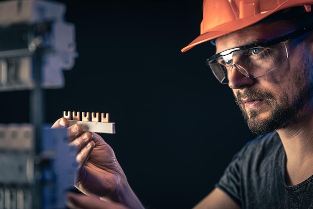 A male electrician works in a switchboard with an electrical connecting cable