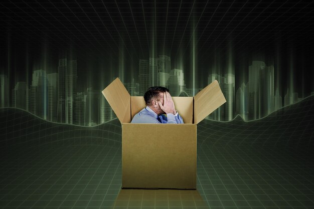 Male employee feeling sad inside a cardboard