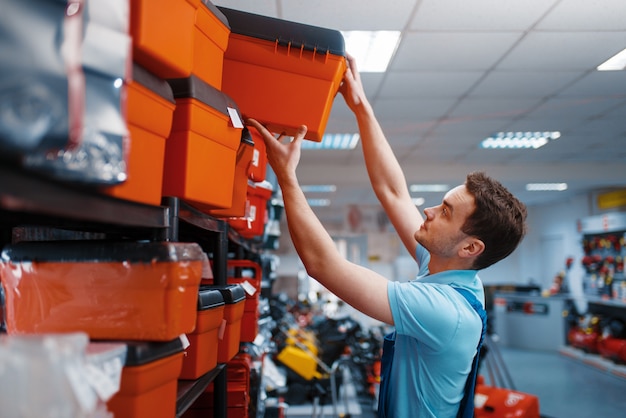 Male employee in uniform choosing toolbox in tool store. Choice of professional equipment in hardware shop, instrument supermarket