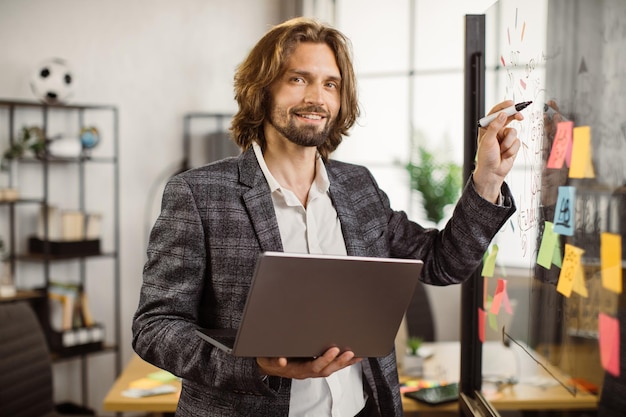 Photo male employee using laptop and office glass board at work