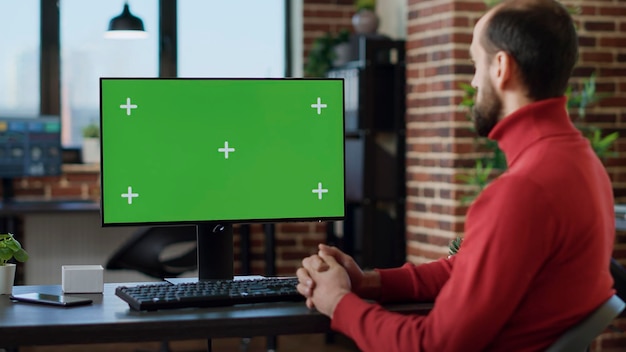 Сотрудник-мужчина работает с зеленым экраном на мониторе, используя технологии за столом Офисный работник анализирует