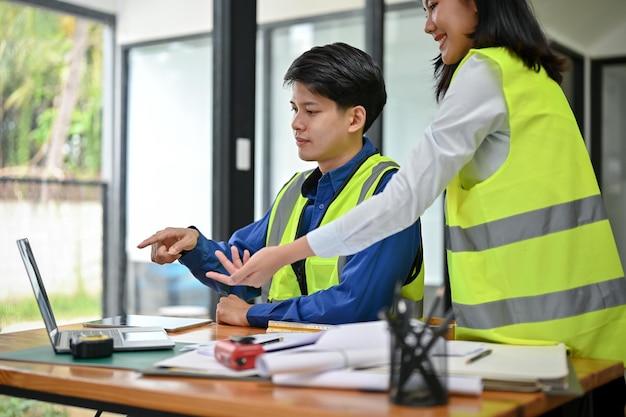 A male engineer is discussing a building blueprint on a desktop with his female colleague