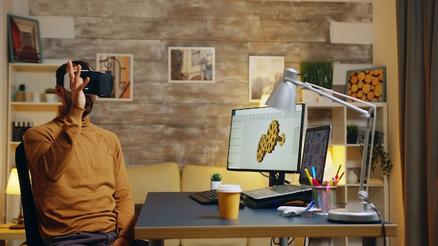 male engineer working in his home office on a new technology for gears system wearing a virtual reality headset.