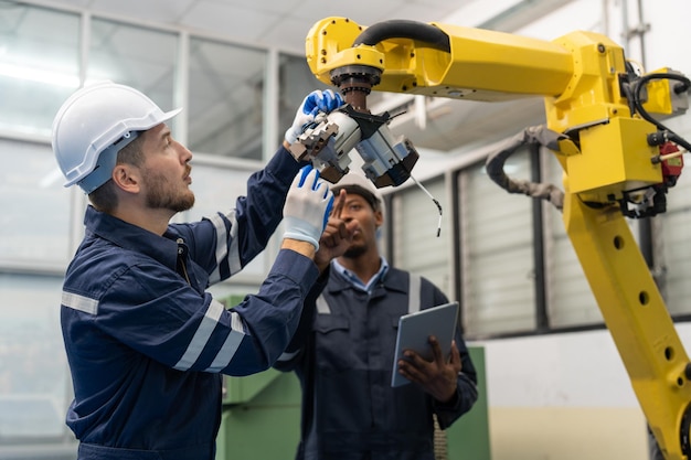 Male engineers wearing vest with helmet safety repairing robot arm welding machine in factory