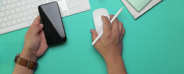 Foto mano destra dell'imprenditore maschio facendo uso del dispositivo del computer e smartphone della tenuta della mano sinistra sul worktable