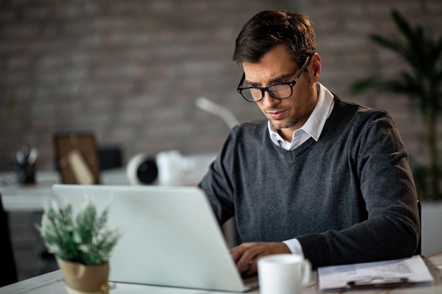 Imprenditore maschio che digita un'e-mail mentre lavora al computer portatile in ufficio