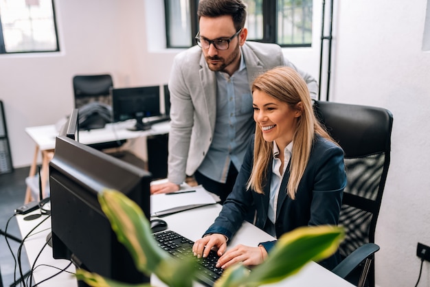 Male executive boss supervising computer work of young female employee.