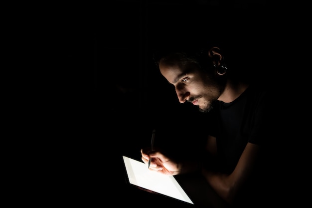 Volto maschile illuminato da uno schermo tablet mentre si utilizza una penna digitale