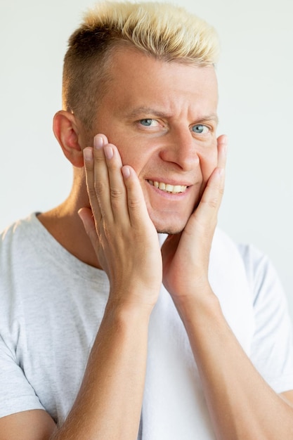 Male facial care Skin irritation Morning grooming Cosmetology procedure Portrait of dissatisfied blond man in white tshirt touching dry cheeks isolated on neutral background