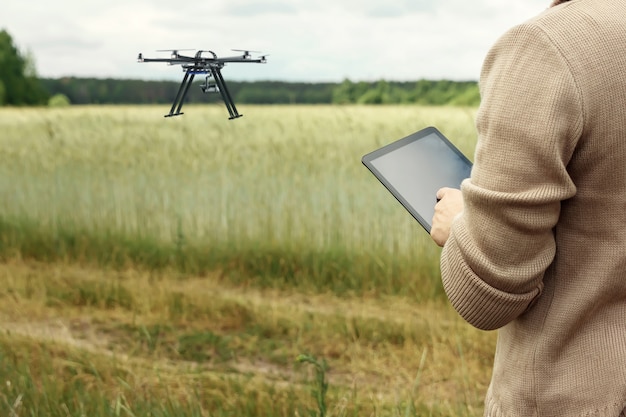 A male farmer manages a drone over agricultural land.