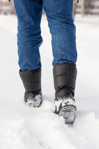 黒のブーツの男性の足、雪の中を歩く冬