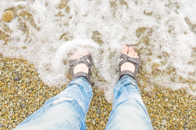 Male feet in sandals in the water at the beach