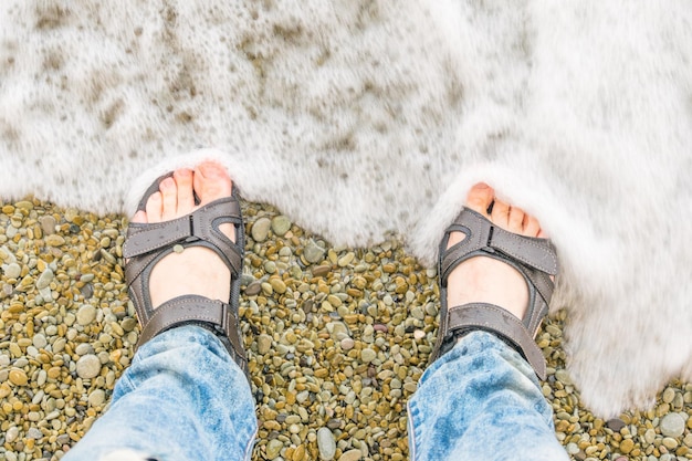 Male feet in sandals in the water at the beach