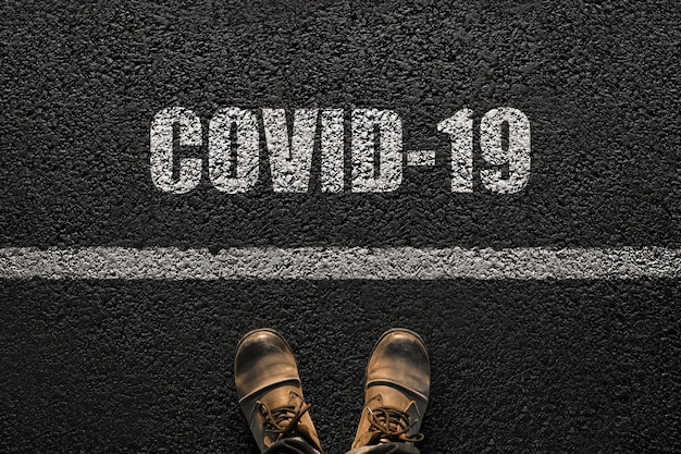 Male feet with boots on the asphalt with the text Covid-19. Humanity and virus concept. Coronavirus and travel