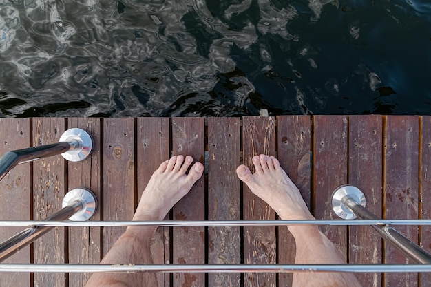 Male feet on a wooden pier Top view of the pier and the water below next to the stainless steel ra