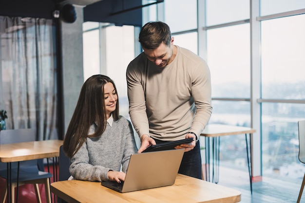 Male and female colleagues work together in a modern office on a project Workers in the office behind the satellite work with a laptop Subordinate and manager