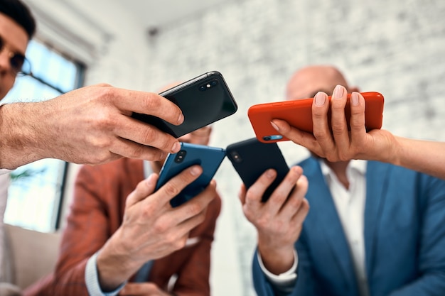 Male and female diverse hands holding cell phones, multiracial business people using smartphones applications software, users and devices concept, mobile communication.