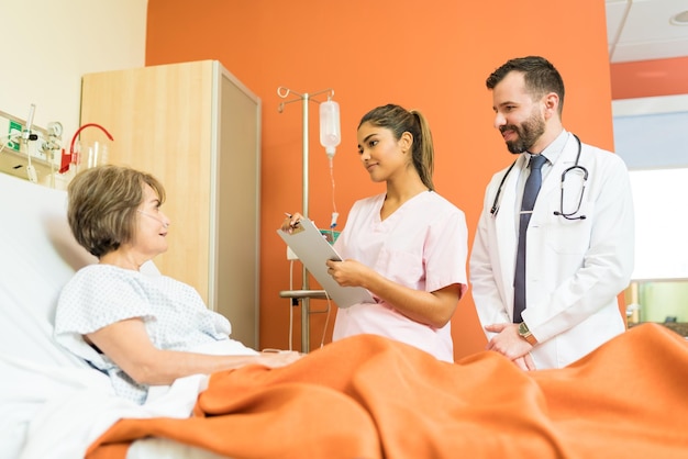 Male and female doctors talking to sick senior patient at hospital