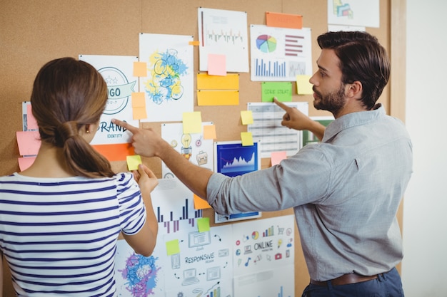 Male and female executives discussing over bulletin board