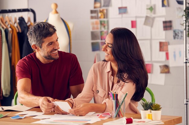 Male And Female Fashion Designers In Studio Working On Sketches And Designs At Desk