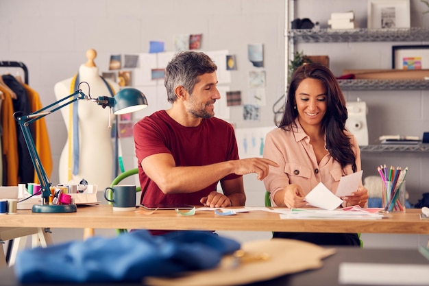 Male And Female Fashion Designers In Studio Working On Sketches And Designs At Desk