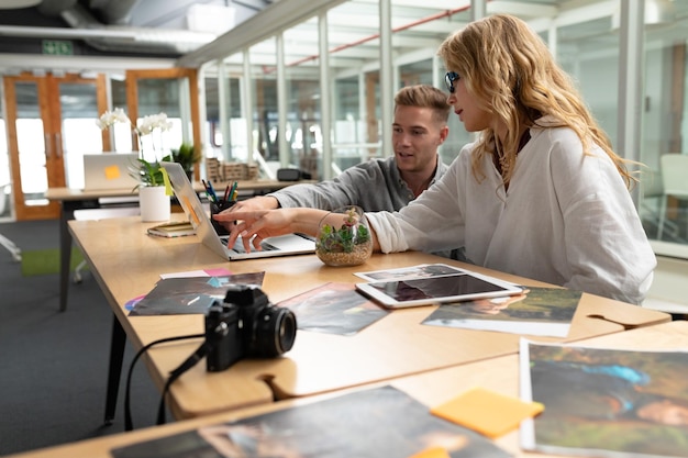 Male and female graphic designers discussing over laptop at desk