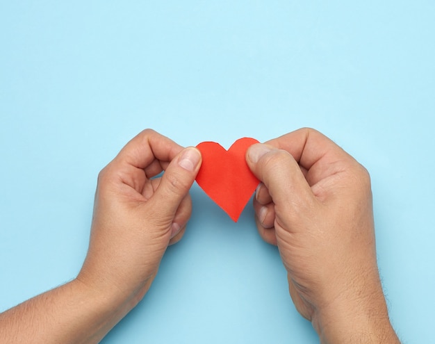 Male and female hand holding red paper heart