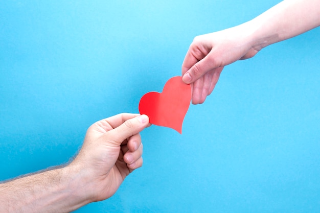 Male and female hands are holding a red paper heart on a blue background