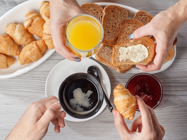 Male and female hands with cup of black coffee and glass of orange juice. Croissants, bread, glass bowl with jam on the background. Top view. Food and beverages for breakfast