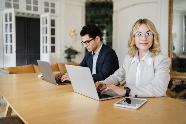 남성과 여성 관리자는 온라인 프로젝트에서 사무실에서 함께 일합니다. 노트북 사용