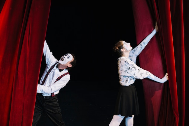 Male and female mime artist pushing opening red curtain